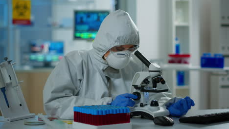 mujer científica en traje de ppe trabajando en el laboratorio usando un microscopio moderno