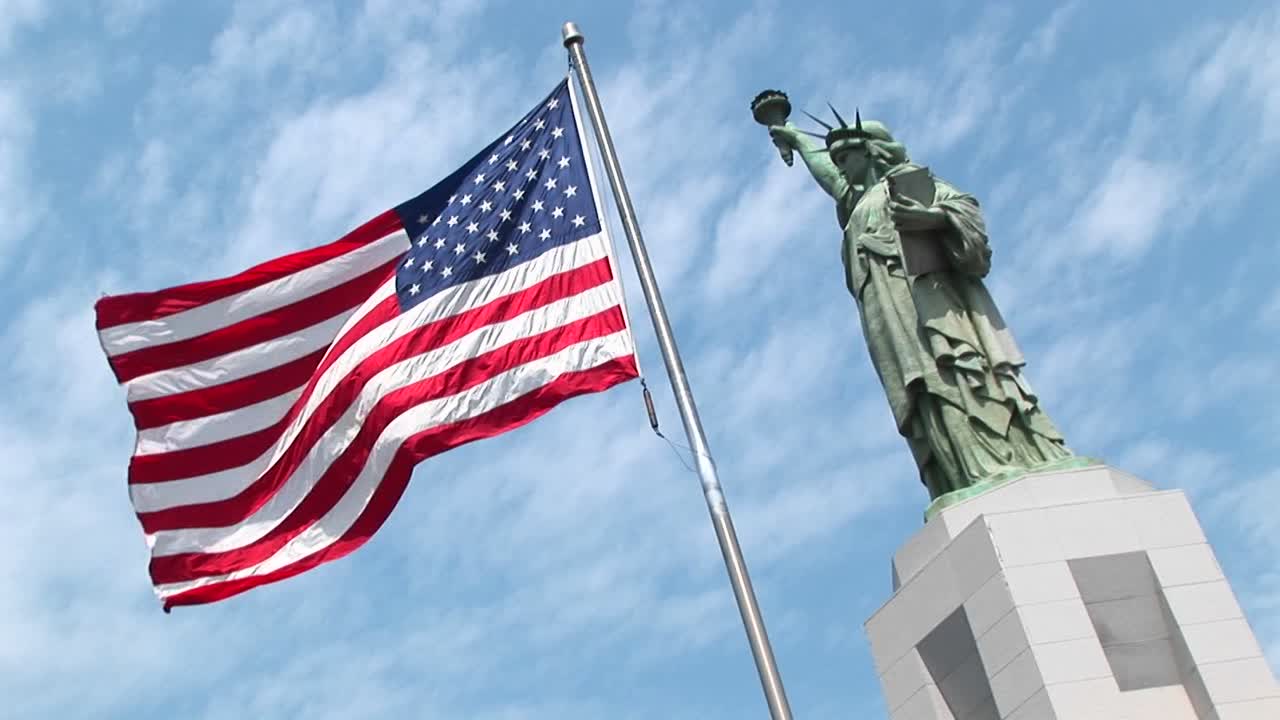 La Statua della Libertà si erge maestosamente sul suo piedistallo mentre una bandiera americana sventola in primo piano.