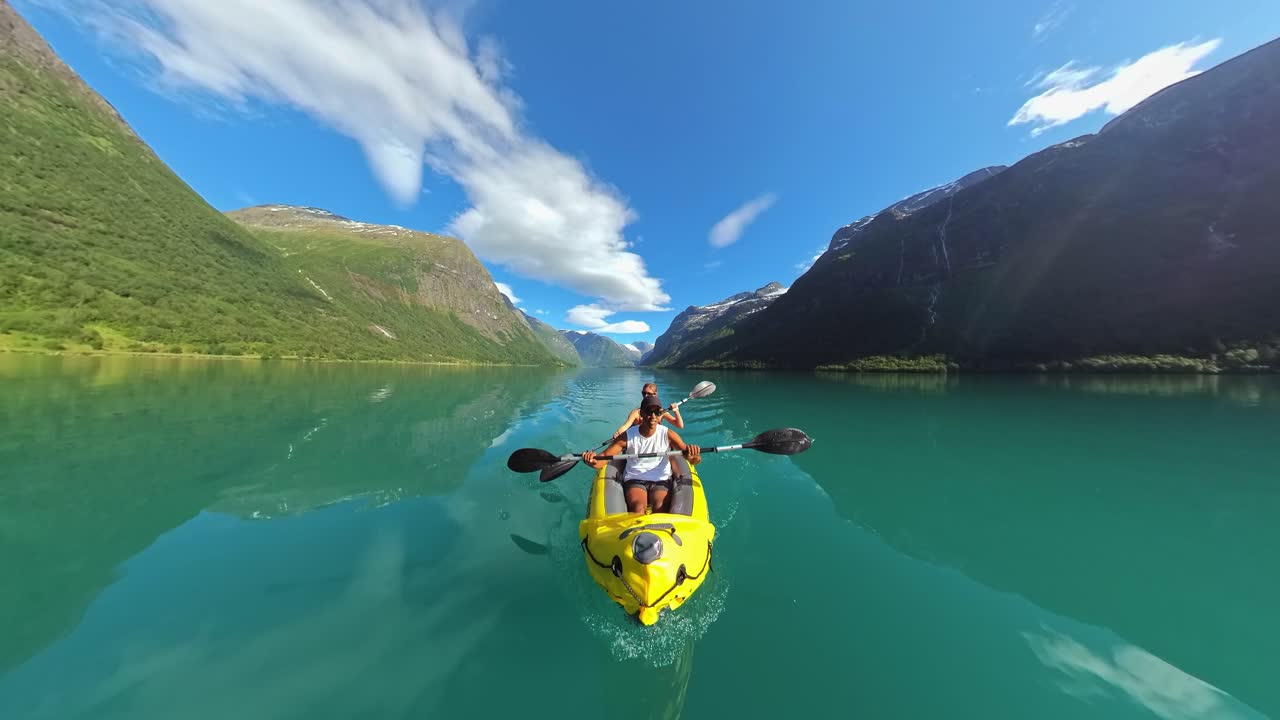 Vista immersiva a 360 gradi della telecamera montata su un kayak, di fronte a una coppia che pagaia attraverso uno splendido fiordo norvegese con acqua turchese, montagne e una luminosa luce solare estiva.