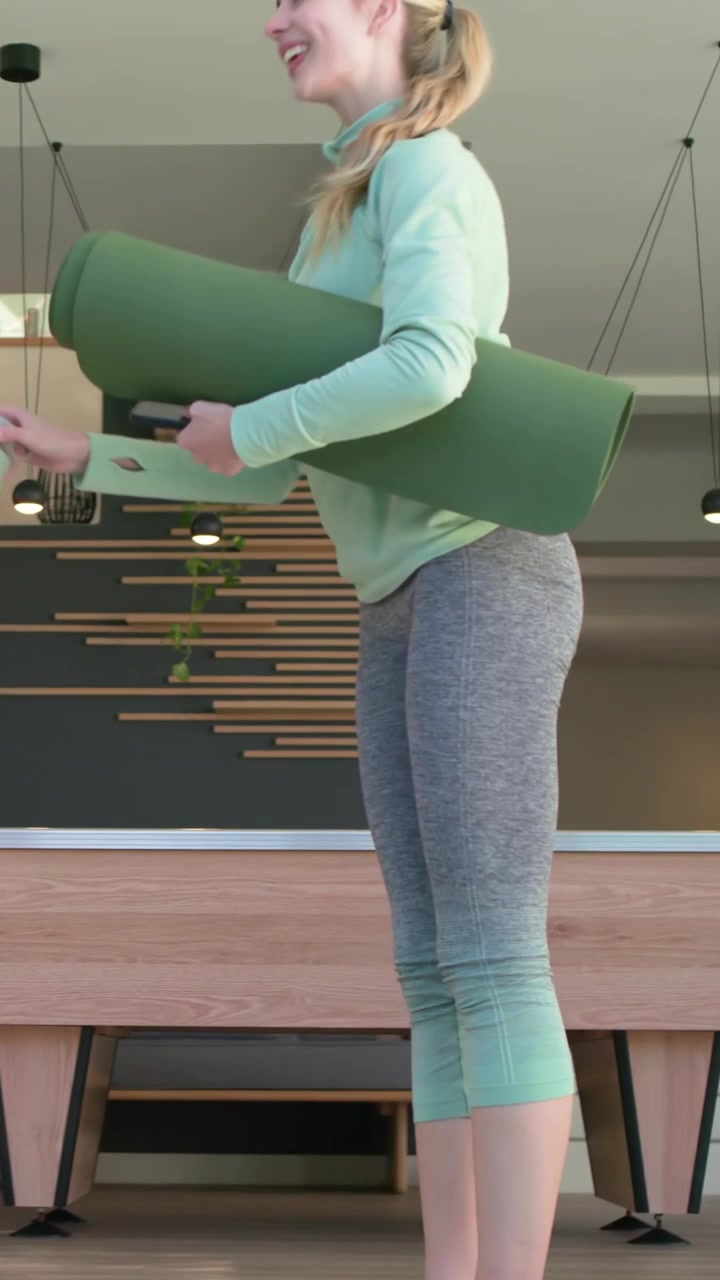 Vertical video: Entering home blond woman in mint top carrying green mat meeting friend practicing