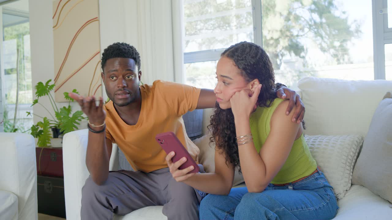 African American couple sitting on white couch, woman reading purple phone and seeking comfort
