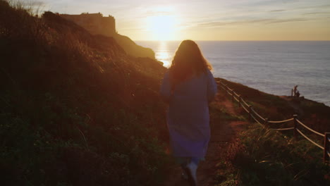 mujer caminando por el camino costero al atardecer