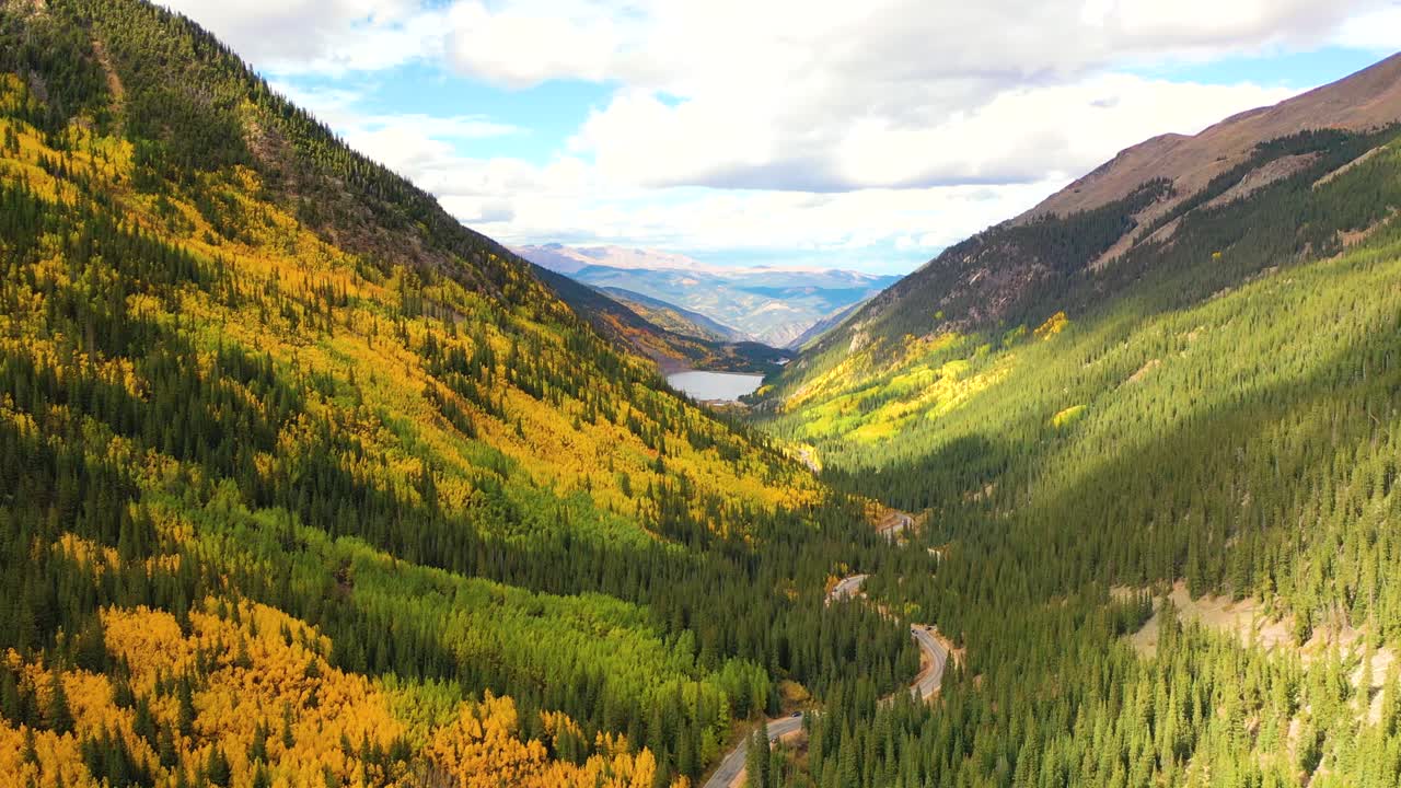 Guanella Pass, Colorado shows rows of cars traveling a high road surrounded by glowing aspens, rugged peaks, and bright sunlight filtering through clouds