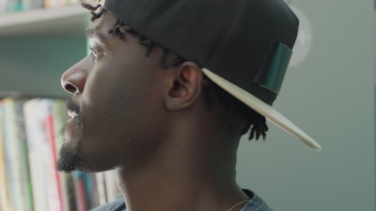 Close up of student in casual wear sorting book on shelf in brightly lit library, surrounded by colorful book spines and blurred background, showing concentration and quiet academic atmosphere