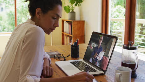 african american woman taking notes while having video call with male colleague on laptop at home