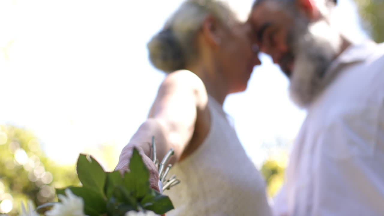 Holding flowers, senior bride and groom hugging at outdoor wedding in park
