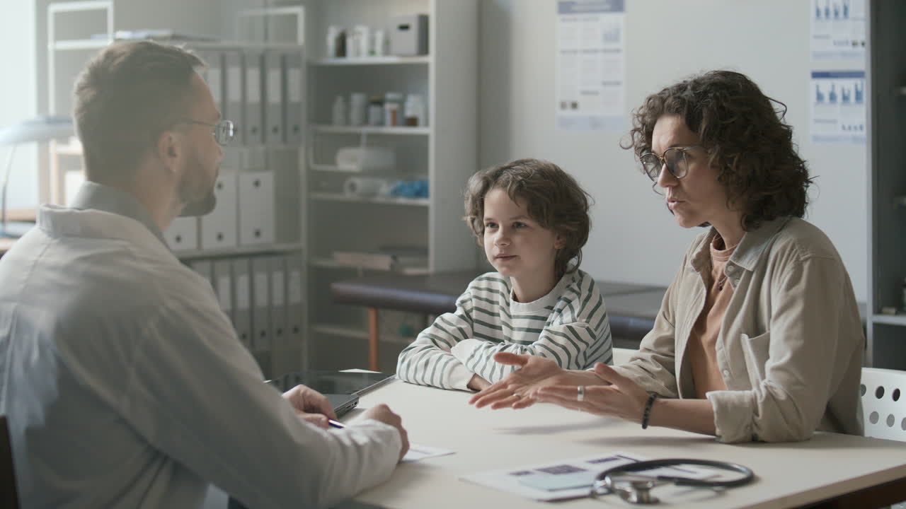 돌보는 어머니와 어린 아들이 소아병원에서 의사와 상담하고 있습니다.