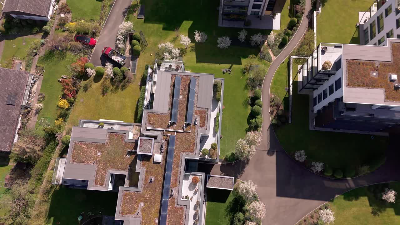 Aerial tilt up of luxury apartment buildings with green vegetated roof and solar panels in Switzerland. Sunny day with green grass and Lake Zurich in background. Wide shot.