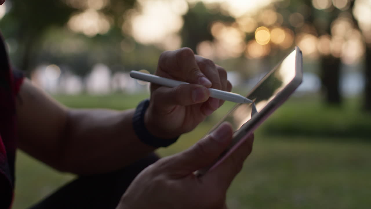 Man Sketching on Tablet in Park at Sunset
