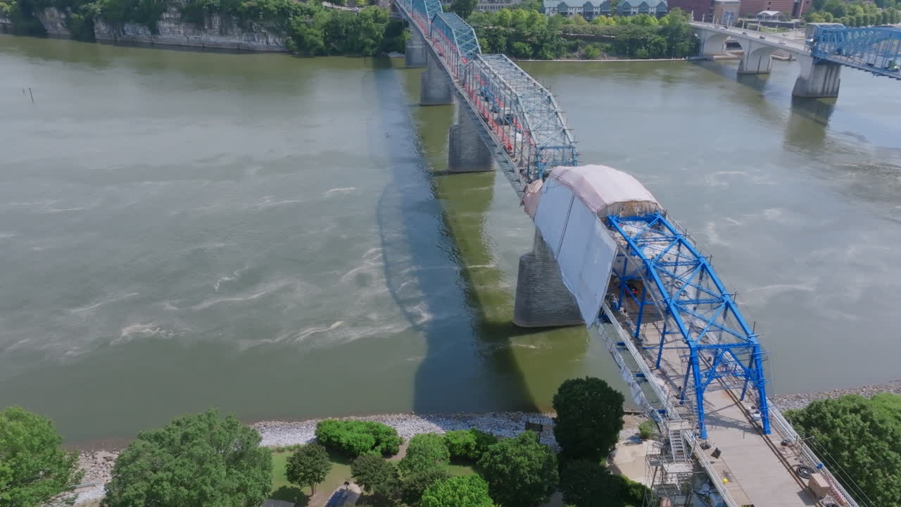 An aerial view of Chattanooga’s Walnut Street Bridge shows it partially covered for maintenance, spanning the Tennessee River with shadows stretching across the water below