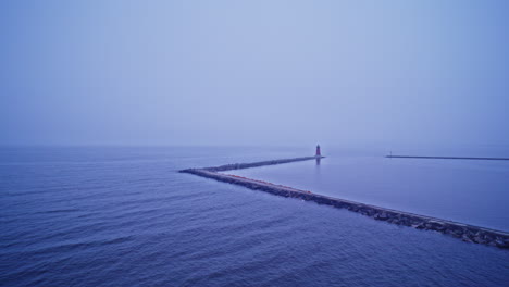 drone shot flying over foggy lake michigan towards lighthouse on the shore of lake michigan