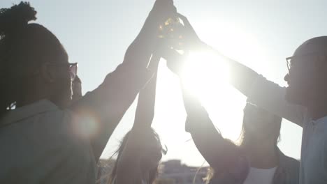 smiling people clinking beer bottles while dancing during sunset