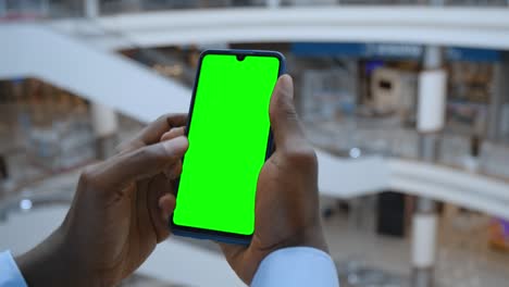 handheld camera: point of view of man at shopping center using phone with green mock-up screen chroma key surfing internet watching content videos blogs tapping on center screen