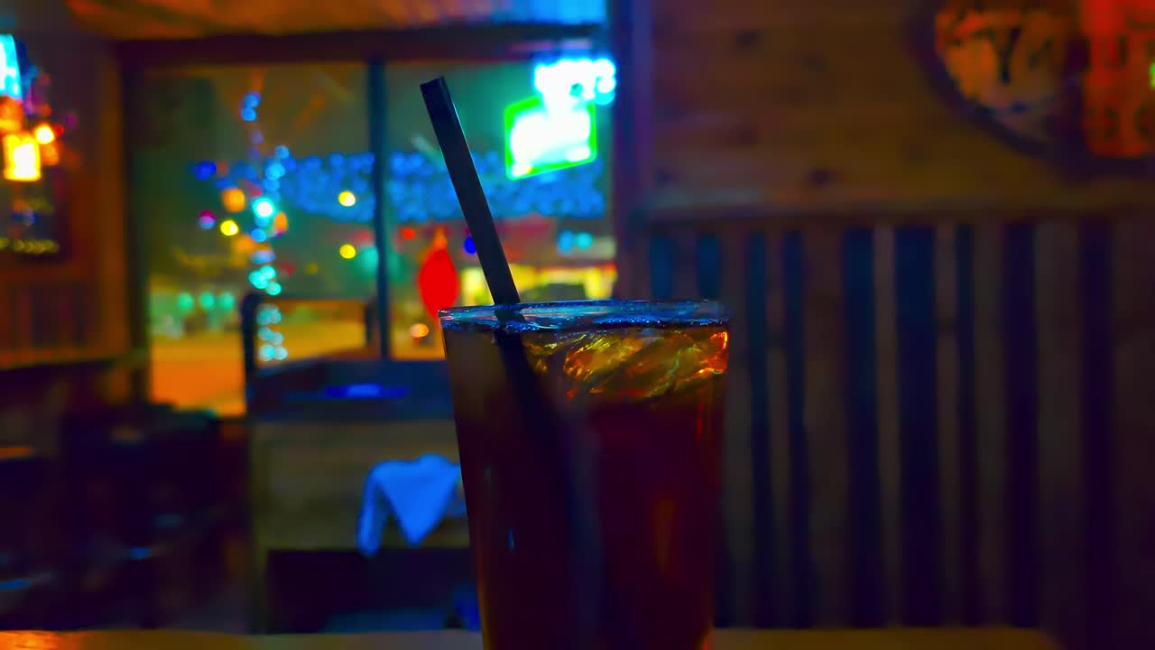 cola soda closeup with pub background dim quiet empty light traffic passing neon lights and tv screens playing with brown walls and oval mirrors at entrance of location at night time