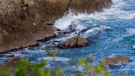 una bandada de gaviotas que vuelan sobre un mar agitado y picado, olas de lavado blanco que se estrellan contra un acantilado rocoso de la costa oceánica