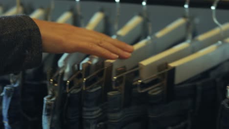 the-woman's-hand-is-hovering-on-the-garment-hanger-on-which-jeans-hang