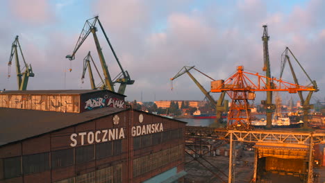 vista aérea de un dron volando sobre el astillero en gdansk al atardecer con grúas en el fondo