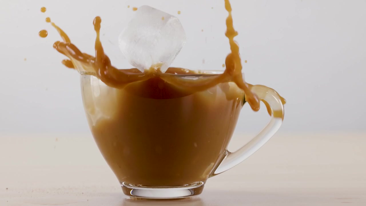 Schizzo al rallentatore mentre un cubetto di ghiaccio cade in una tazza di caffè di vetro su sfondo bianco