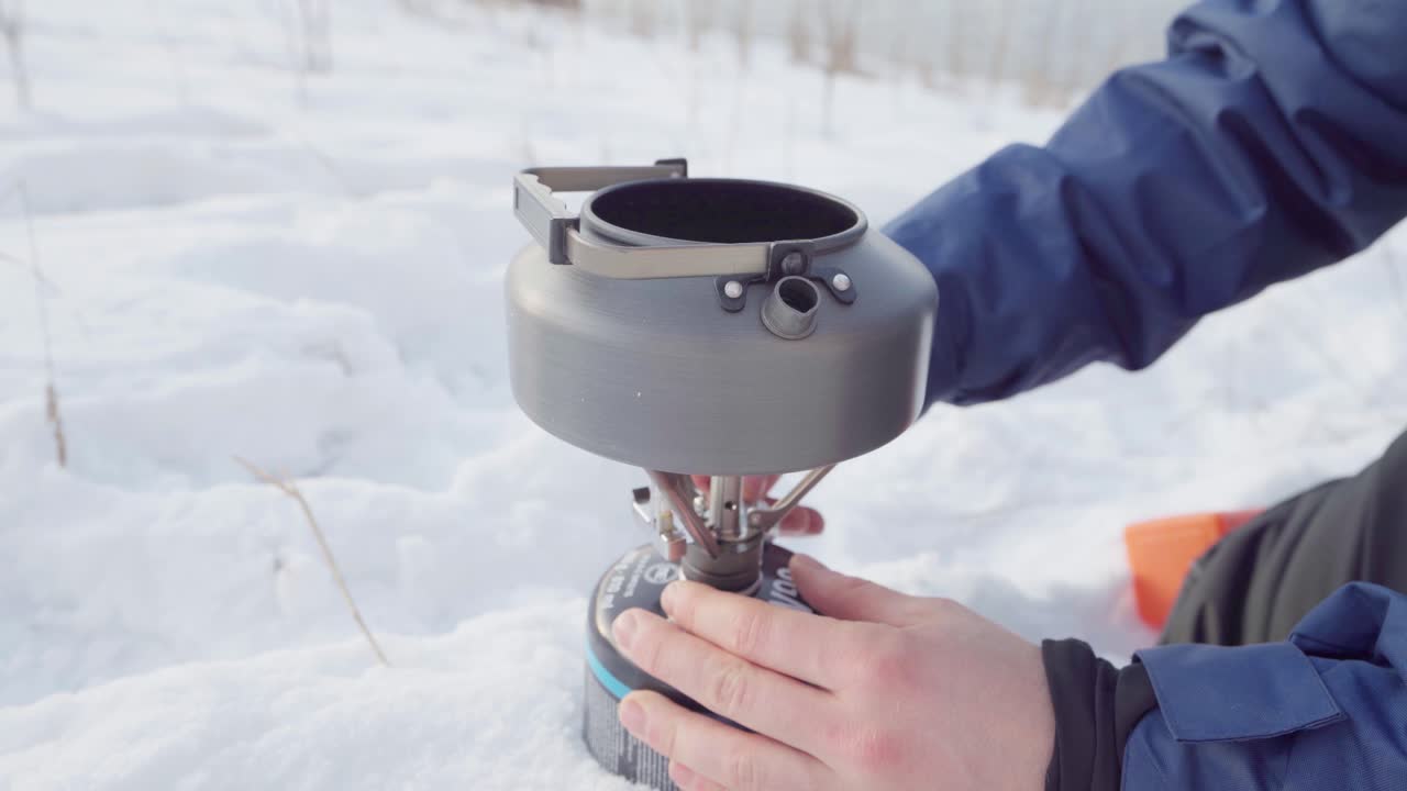 스테인리스 찻주전자가 있는 단일 휴대용 캠핑 스토브를 조이는 남자의 손