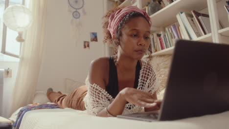 young black girl lying on bed and using laptop