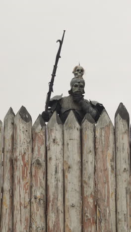 dark knight with skull on helmet peeks behind high wooden fence on cloudy rainy day. monster in armor looks for enemies in medieval village low angle shot