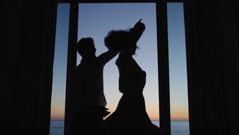 silueta pareja feliz bailando en la habitación del hotel al atardecer disfrutando de las vacaciones de luna de miel divirtiéndose celebrando en vacaciones con una hermosa vista al océano