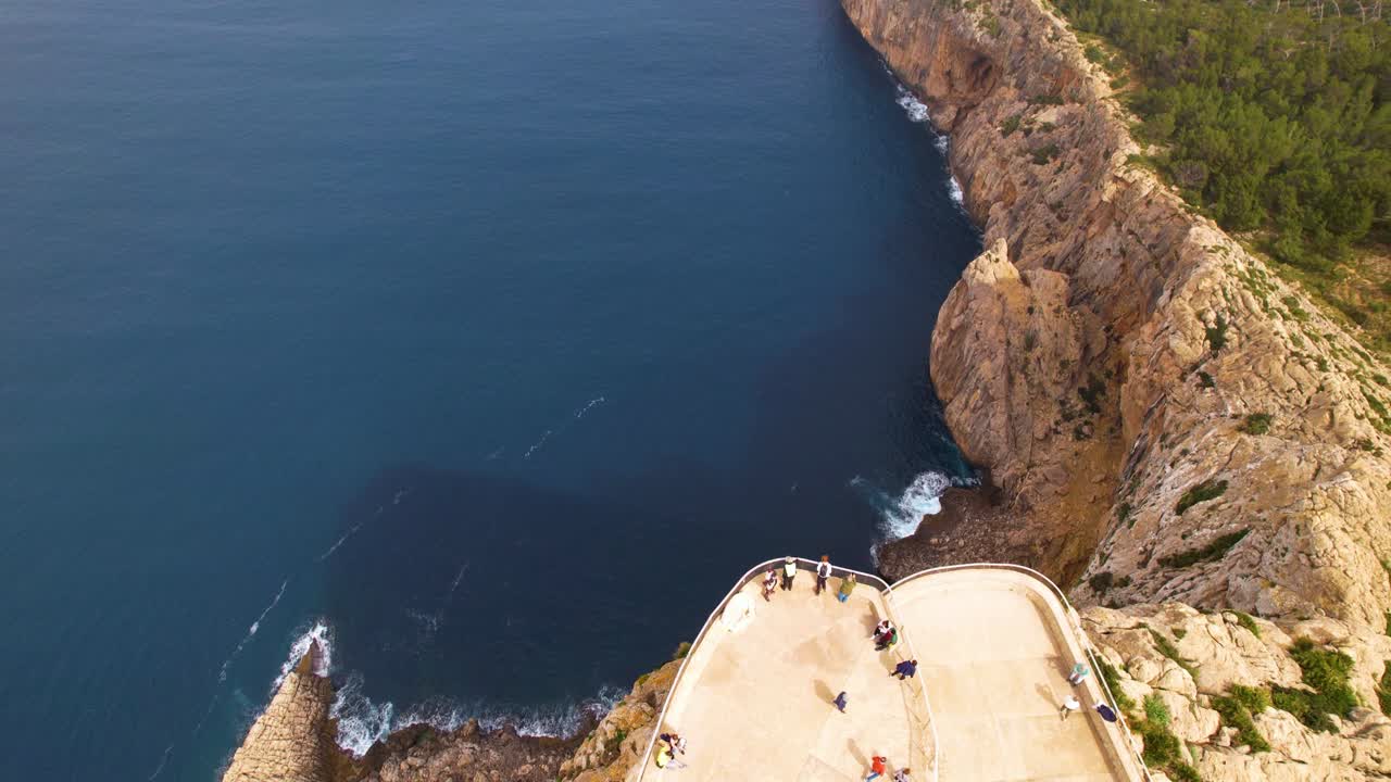 A cliff with a path leading to a viewpoint. Tourists enjoy the view at Cap de Formentor