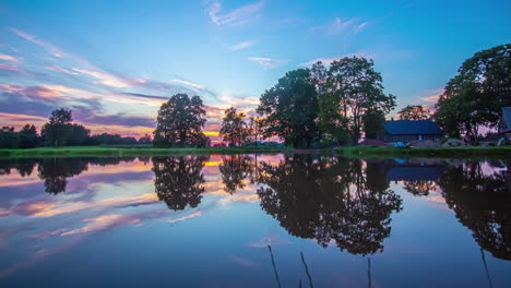 golden sunset above a cabin by a lake with the scene reflecting off the water's surface - time lapse