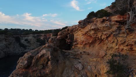 Woman-doing-some-yoga-during-sunset-in-the-cliffside-of-Ibiza,-Spain