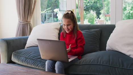 caucasian girl having a video chat on laptop while sitting on the couch at home