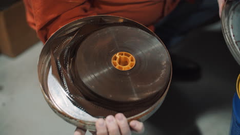 a man opens an old metal round box with an old film strip inside