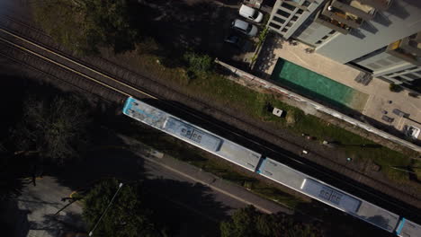 Gray-blue-train-rides-on-rails,-railway-tracks-near-the-house,-top-view