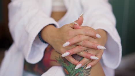 Woman-with-manicure-and-tattoos-on-leg-in-gown-sits-in-room