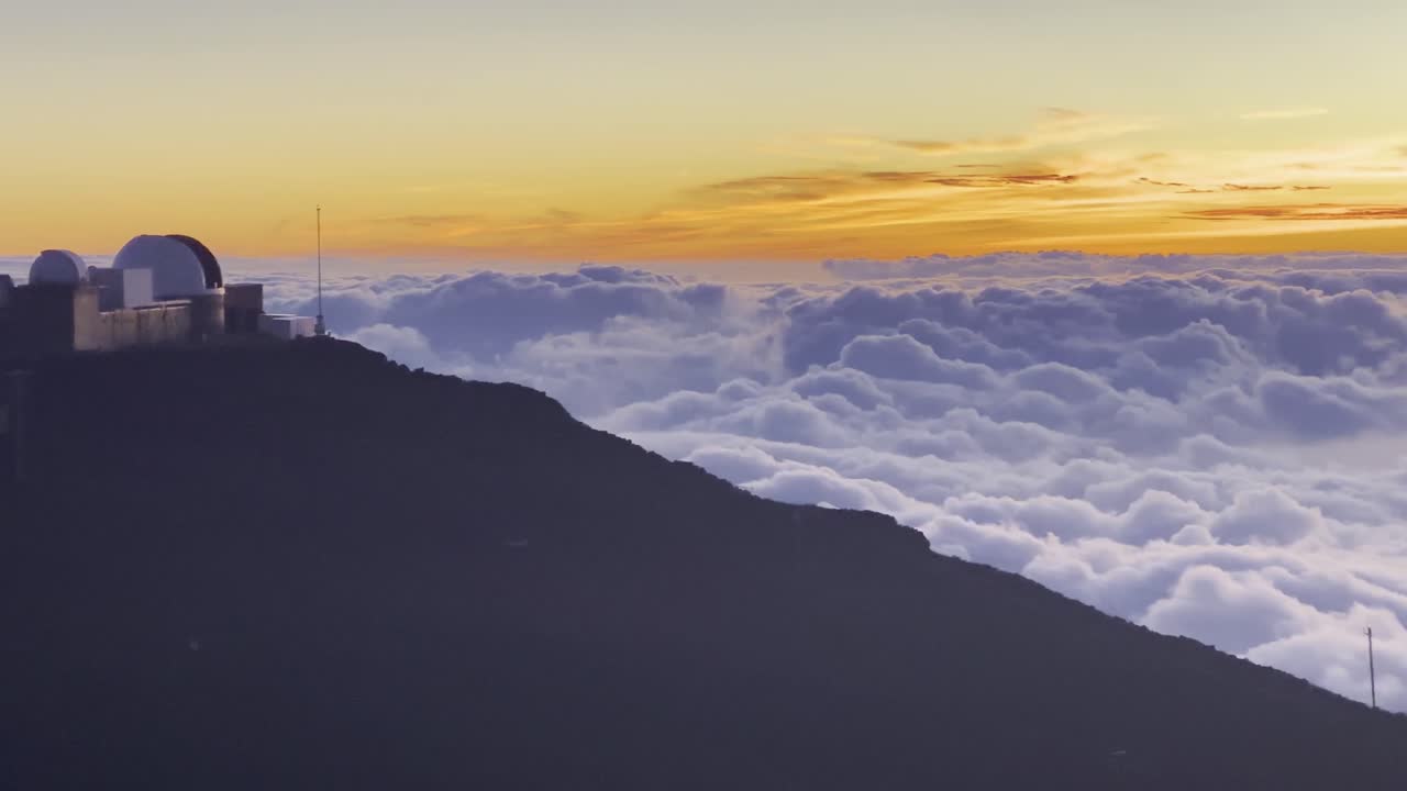 Cinematic panning shot from the Haleakala Observatory to the rolling clouds below the summit of Haleakala at sunset in Maui, Hawai'i