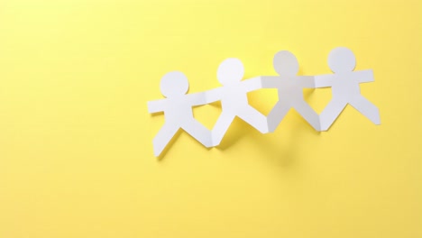 close up of people holding hands made of white paper on yellow background with copy space