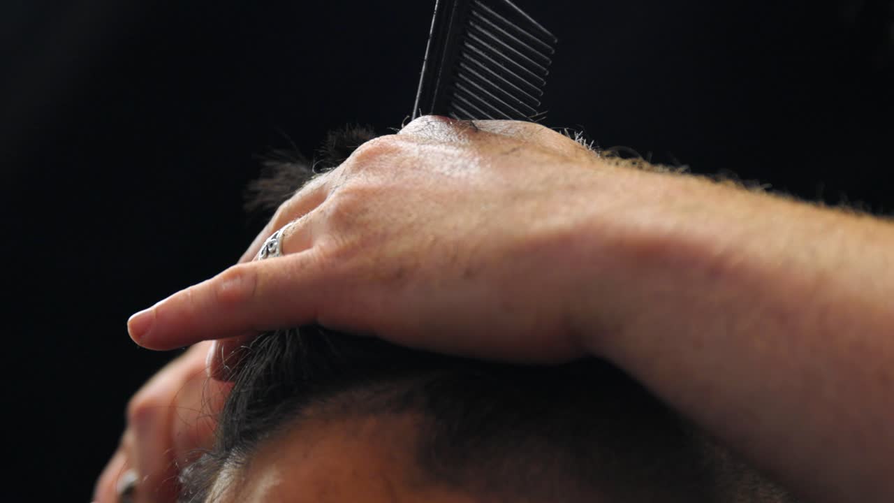 barbiere per capelli che pettina la parte superiore dei capelli dell'uomo, tenendoli sollevati, quindi tagliando le punte con le forbici