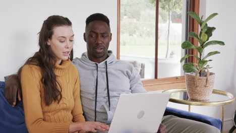 Happy-diverse-couple-sitting-on-sofa-and-using-tablet-in-home,copy-space