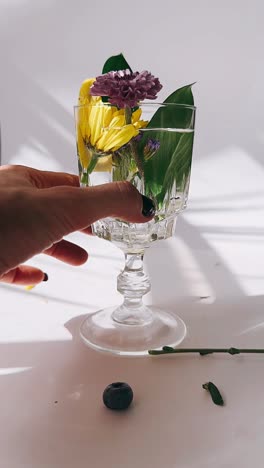 hand holding a glass of water with flowers and lemon