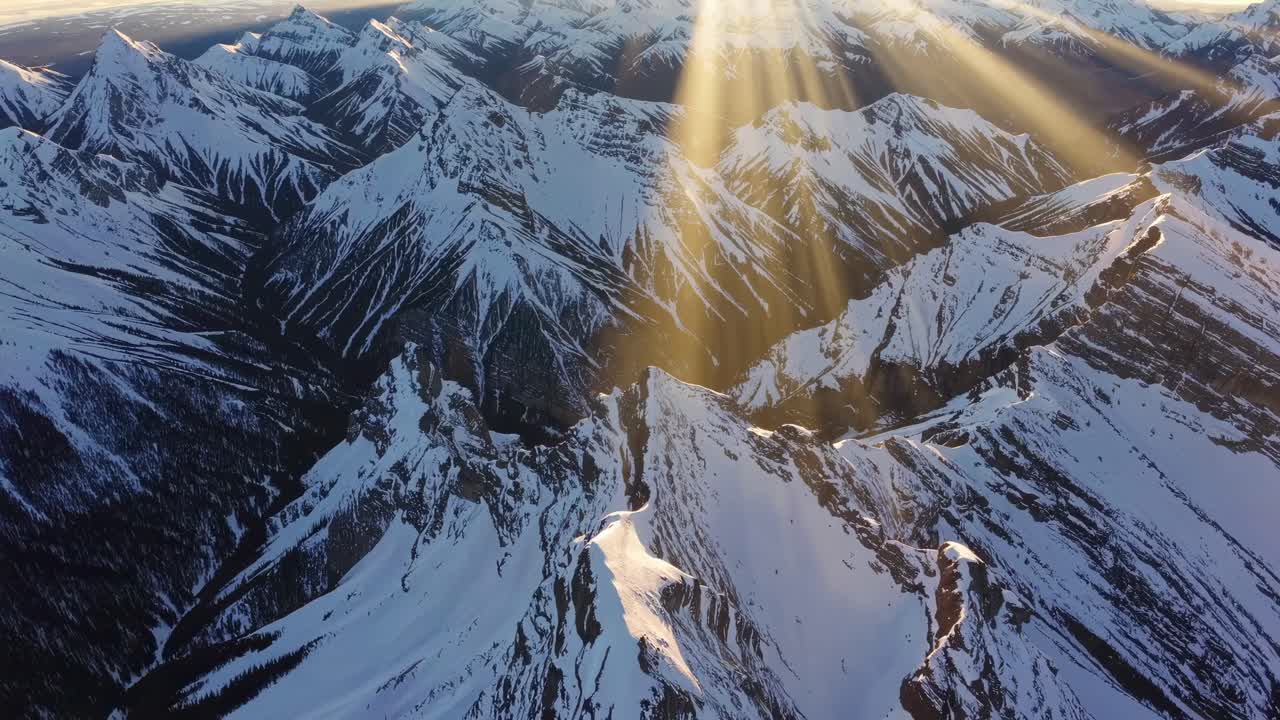 Aerial video captures snow-capped mountains with sun rays streaming through clouds
