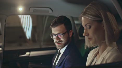 Outside-View-Of-A-Moving-Car,-A-Couple-In-Smart-Clothes-Talk-While-Looking-At-Smartphone