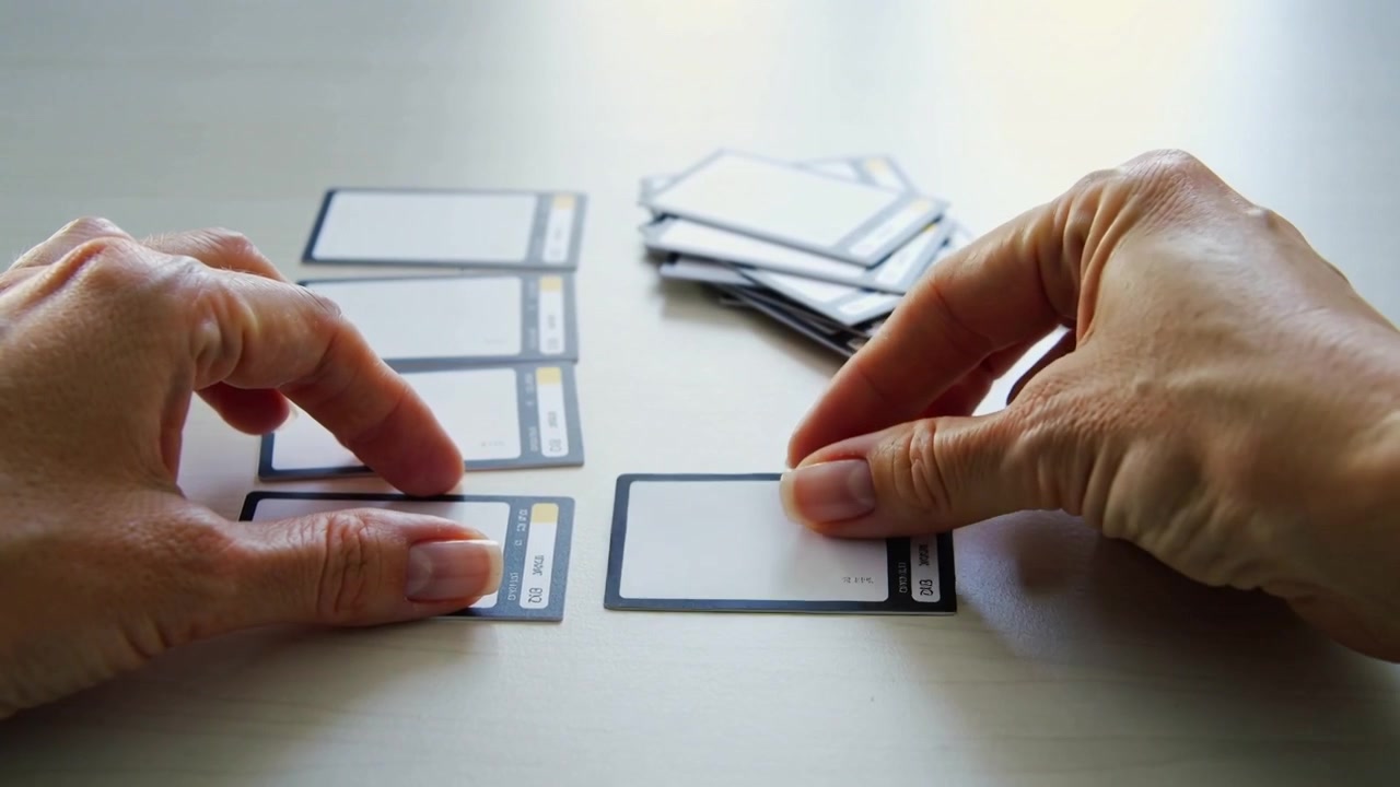 Picking card from pile, hands placing, aligning rectangular cards on light table for layout