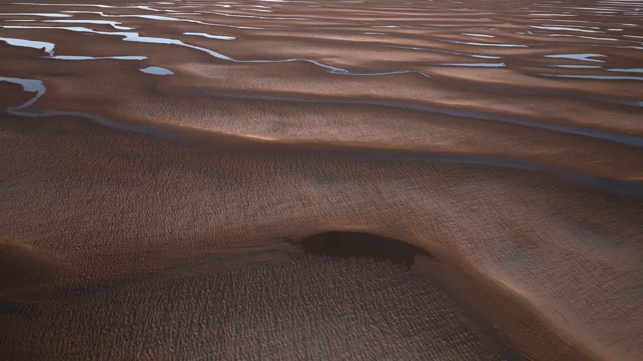 Fast flight over undulating sand patterns catching sunset light with seawater pools.