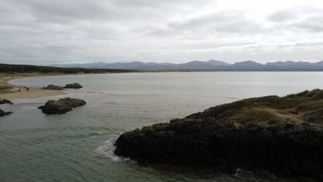 aerial view orbiting ynys llanddwyn island anglesey coastal walking trail with snowdonia mountains across the irish sea