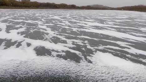 slow panning shot of cold blowing snow accumulating along cracks in ice as the water freezes