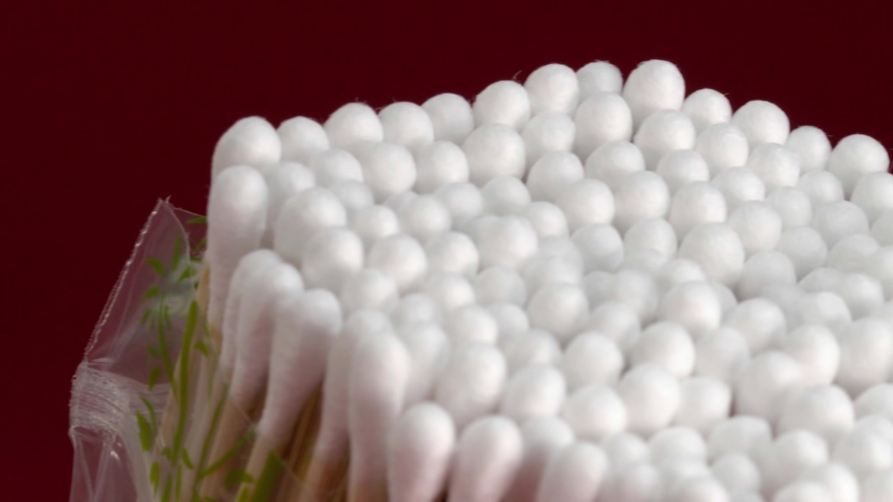 Primo piano in panoramica a sinistra di cotton fioc raggruppati con morbide punte di cotone bianco, che creano un motivo pulito e ripetuto su uno sfondo rosso. Prodotto per l'igiene quotidiana e la cura personale.
