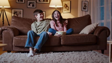 happy children watching tv and eating popcorn on a couch