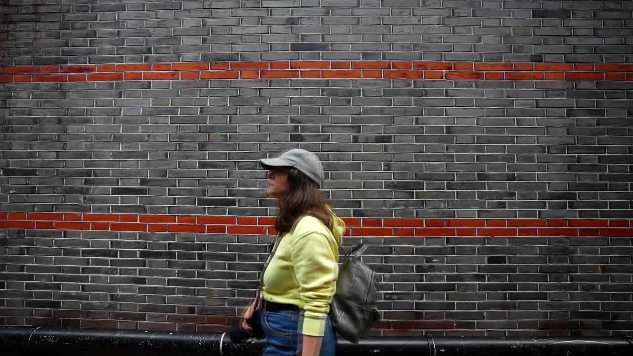 Tourist woman walks past a grey brick wall accented by red trim in the Xintiandi neighborhood. Shanghai, China