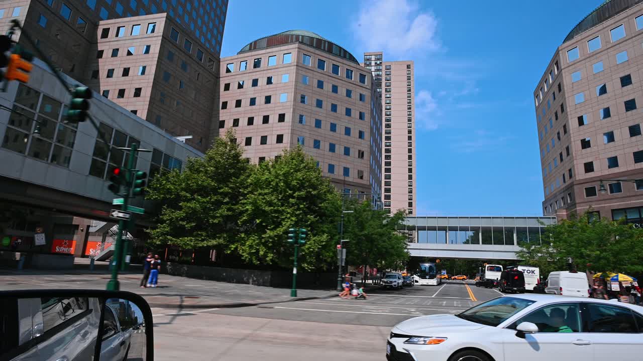 New York, USA, 9 agosto 2025: Auto berlina bianca che passa davanti a un grande edificio moderno per uffici. Vista laterale di un veicolo bianco su una strada urbana con una facciata in pietra contemporanea a più piani.