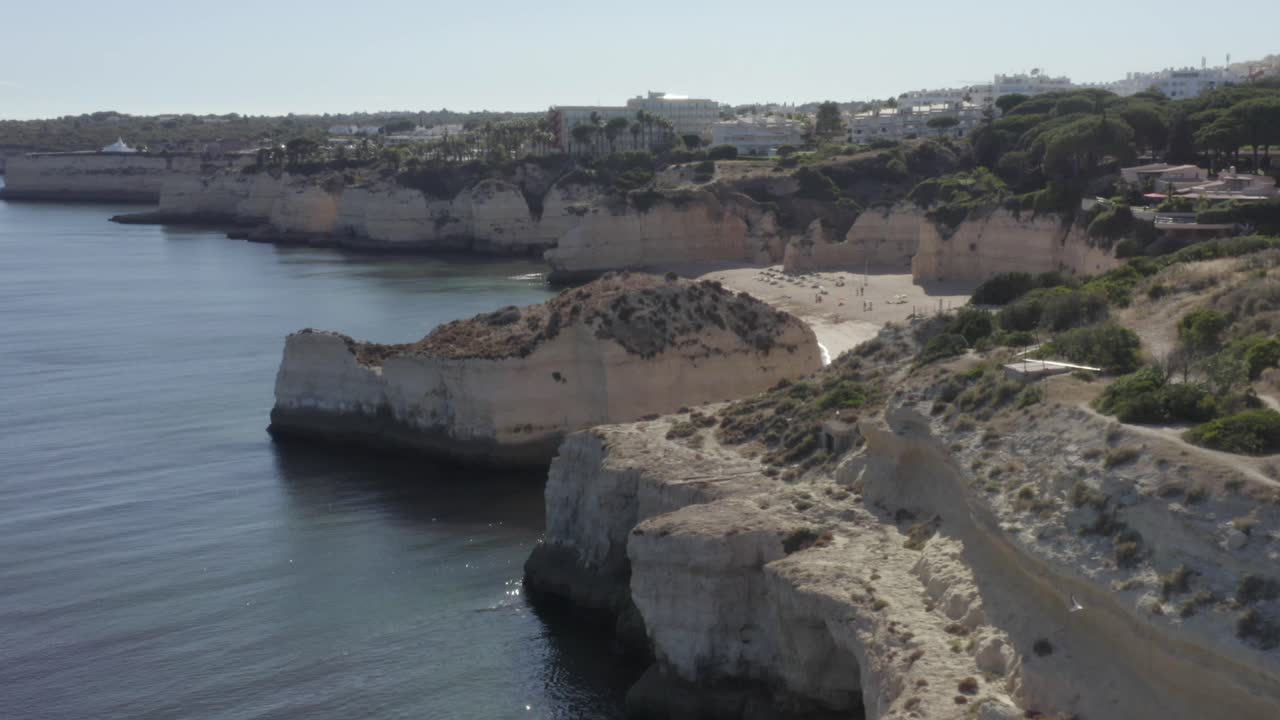 el dron vuela alrededor del épico acantilado oceánico revelando toda la playa escondida rodeada de acantilados y formaciones rocosas en aguas tranquilas y tranquilas
