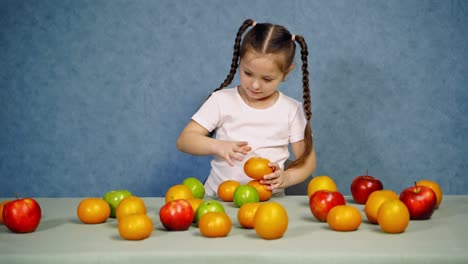 lovely little girl plays with fruit. bright organic fruit on the table. amazing child making tower of fresh tangerines on blue background.